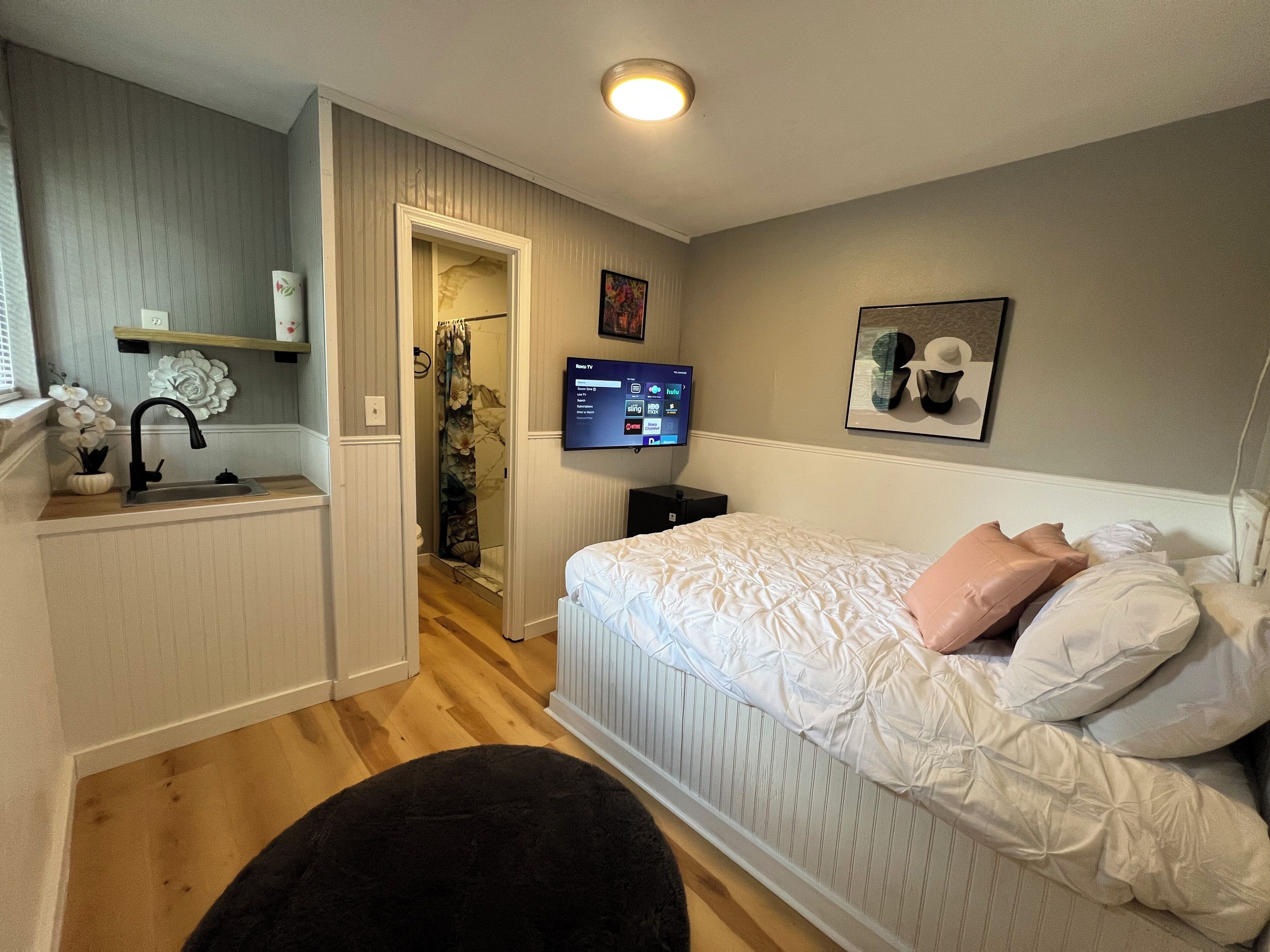 A bedroom with a bed, a TV, a bathroom, and a small kitchenette.