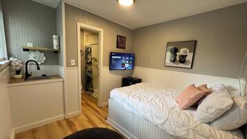 Un dormitorio con cama, televisión, baño y una pequeña kitchenette.