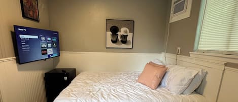 A bedroom with a bed, a television mounted on the wall, and a window with blinds.