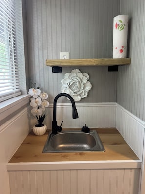 Una cucina con un lavello in acciaio inossidabile, un rubinetto nero, un vaso bianco con fiori e un elemento decorativo a parete.