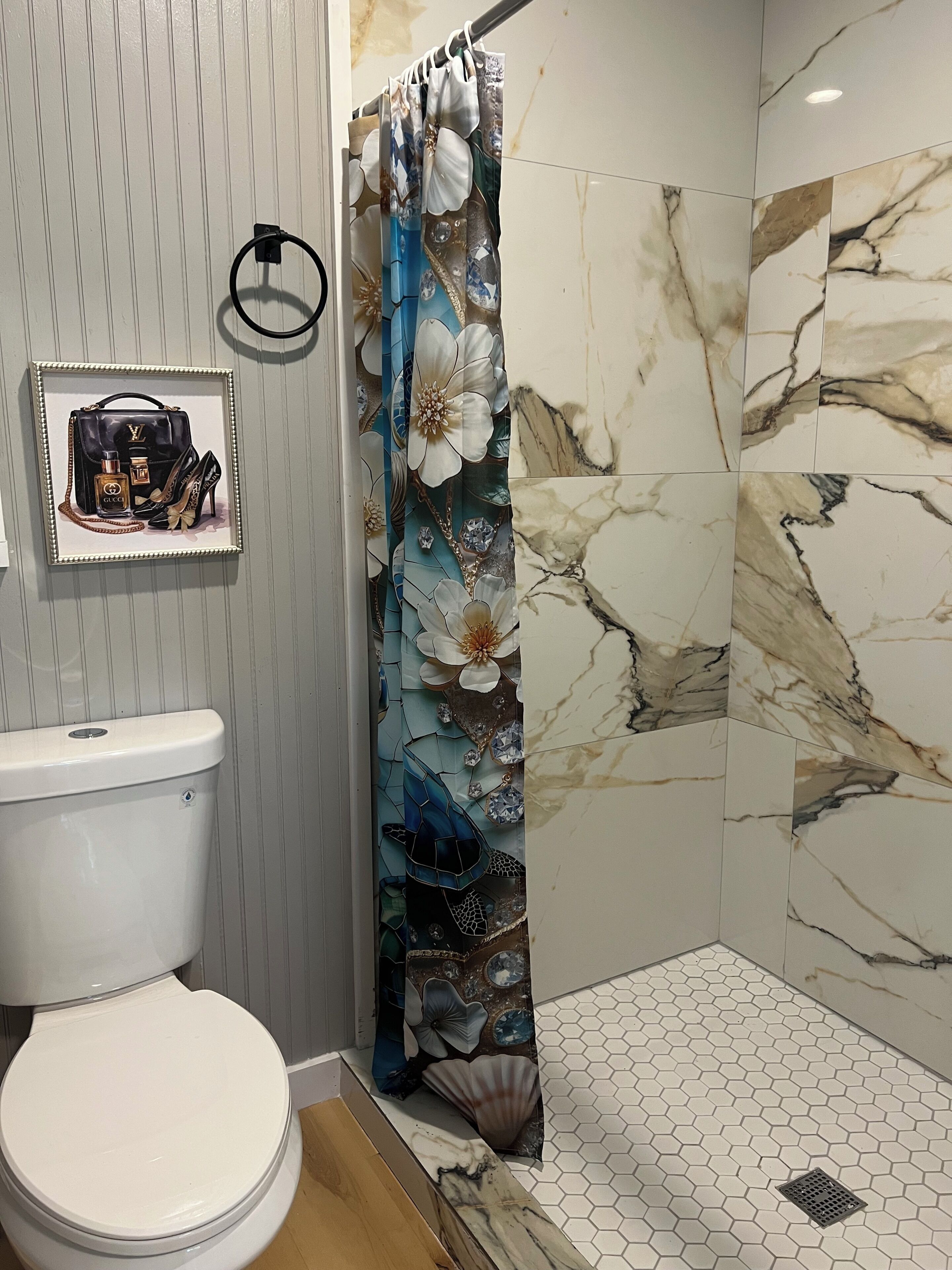 Een badkamer met toilet, een douche met bloemen gordijn en een lijst met foto aan de muur.