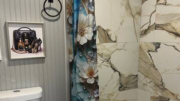 Een badkamer met toilet, een douche met bloemen gordijn en een lijst met foto aan de muur.