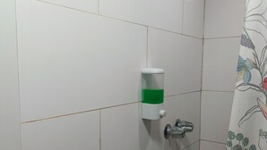 A shower area with white tiles, a green soap dispenser, and a showerhead.