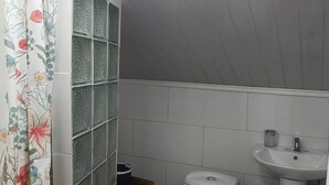 A bathroom with a toilet, a sink, a shower area with tiled walls, and a small wicker basket on a stool.