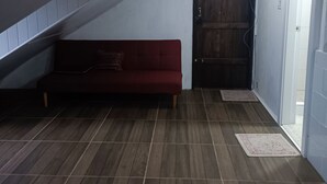 Une pièce avec un plafond en pente, une porte en bois, un canapé rouge et un sol carrelé.