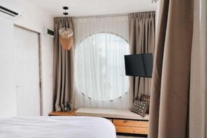 A bedroom with a bed, a window with curtains, a television, and a bench.
