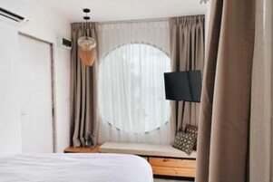 A bedroom with a bed, a window with curtains, a television, and a bench.