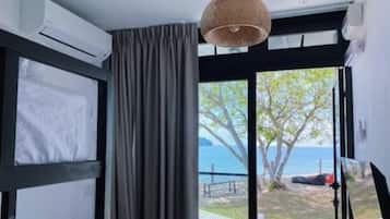 A room with a bed, a window with a view of the sea, and an air conditioning unit.