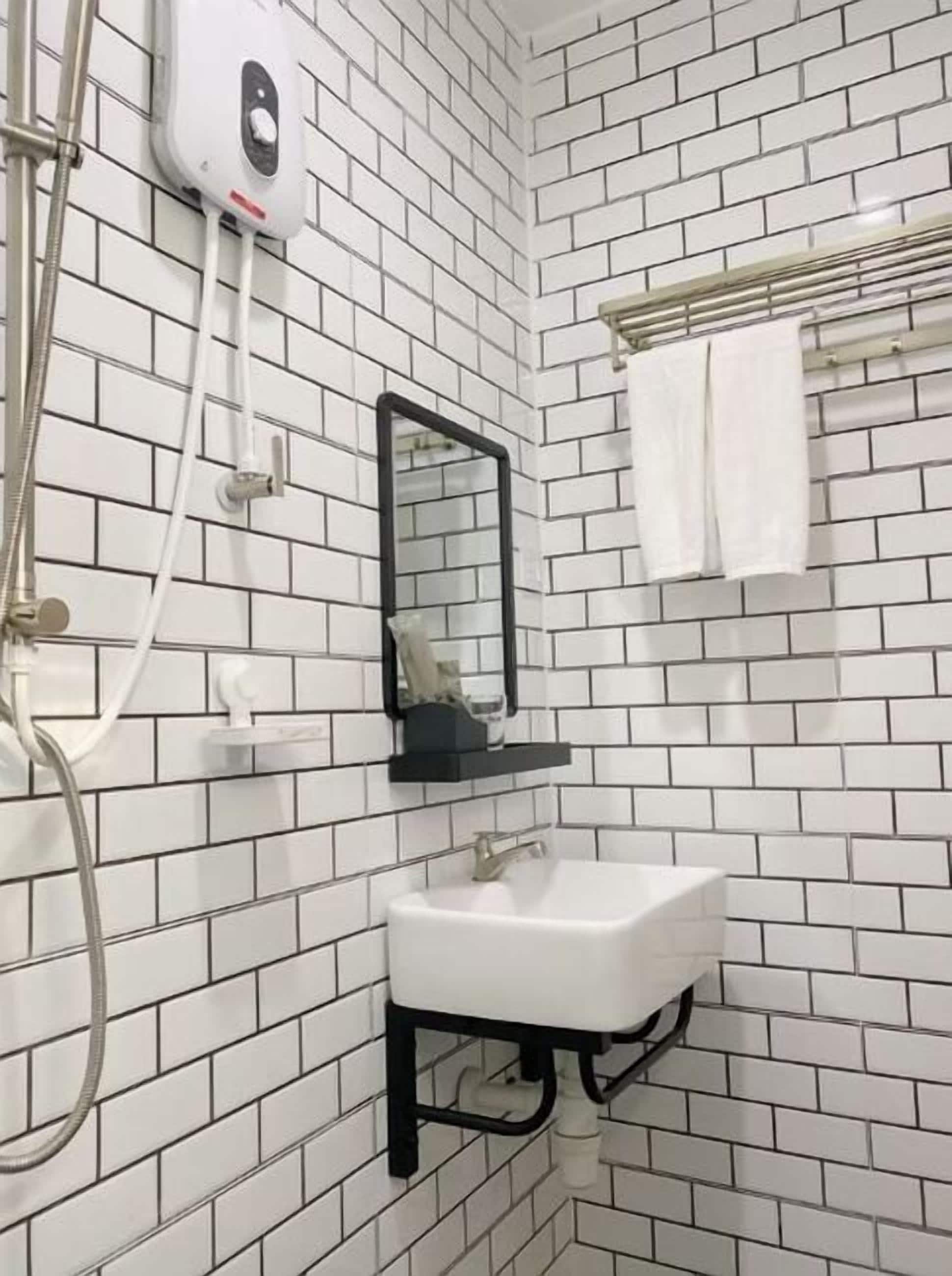 A bathroom with white tiled walls, a white sink, a black-framed mirror, and a towel rack with a white towel.