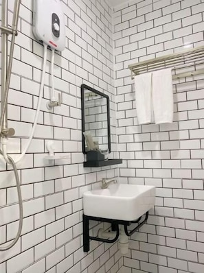 Un baño con paredes de azulejos blancos, un lavamanos blanco, un espejo con marco negro y un perchero con una toalla blanca.