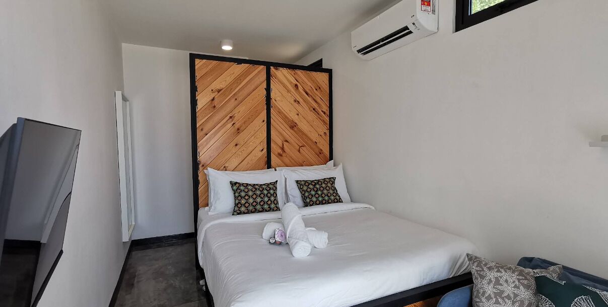 A hotel room with a bed, a television, a wardrobe, and an air conditioning unit.