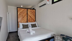 A hotel room with a bed, a television, a wardrobe, and an air conditioning unit.