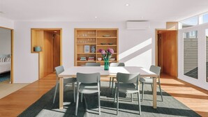 A modern dining room with a white table, grey chairs, and a wooden bookshelf. - Bondi Penthouse with Panoramic Views (Bondi)
