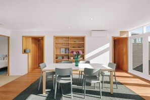Ein stilvolles Esszimmer mit einem weißen Tisch, grauen Stühlen und einem Holzregal.