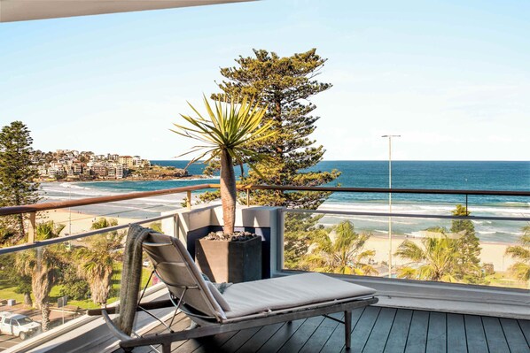 A balcony with a view of a beach and ocean, a lounge chair, and a potted plant. - Bondi Penthouse with Panoramic Views (Bondi)