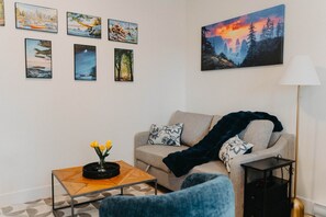 A living room with a sofa, a coffee table, and a lamp. There are six framed pictures on the wall. - Cozy Modern 1BR Suite, Workspace, Laundry & Coffee (Langford)