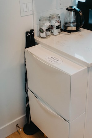 Eine kompakte Küche mit einem weißen Kühlschrank, einer Kaffeemaschine und Gläsern auf der Arbeitsplatte.