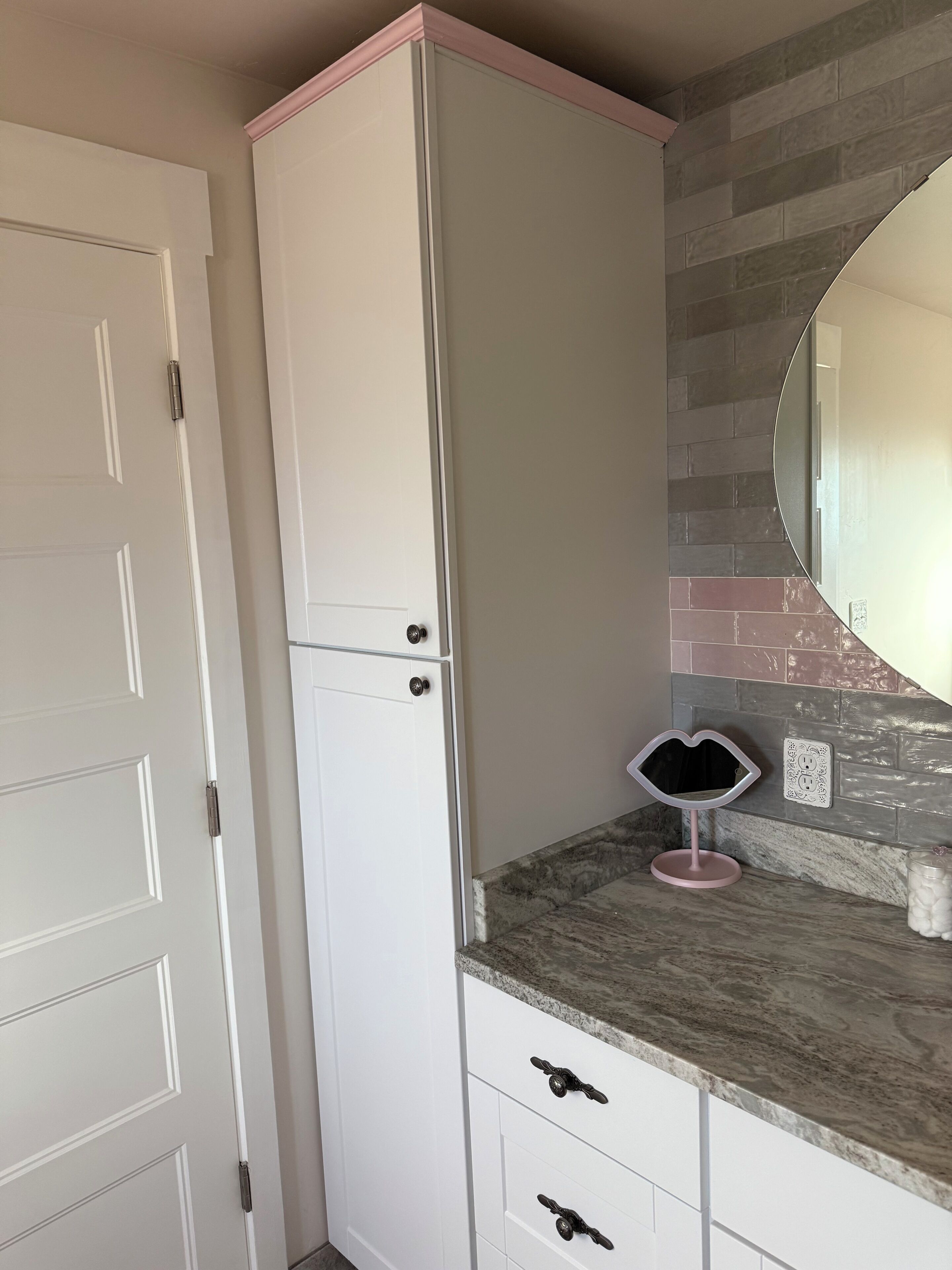 Een badkamer met een wit wastafelmeubel, een spiegel en een betegelde spatwand.