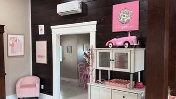 A room with a wooden ceiling, a disco ball, a pink toy car, and a white cabinet with drawers.