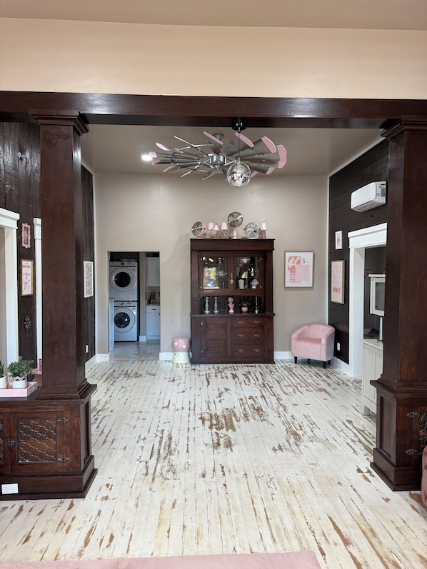 A room with a wooden floor, a ceiling fan, a disco ball, a cabinet with glass doors, and a washing machine in the background.