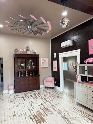 Une pièce avec un ventilateur de plafond, une boule à facettes, un meuble en bois et une chaise rose.