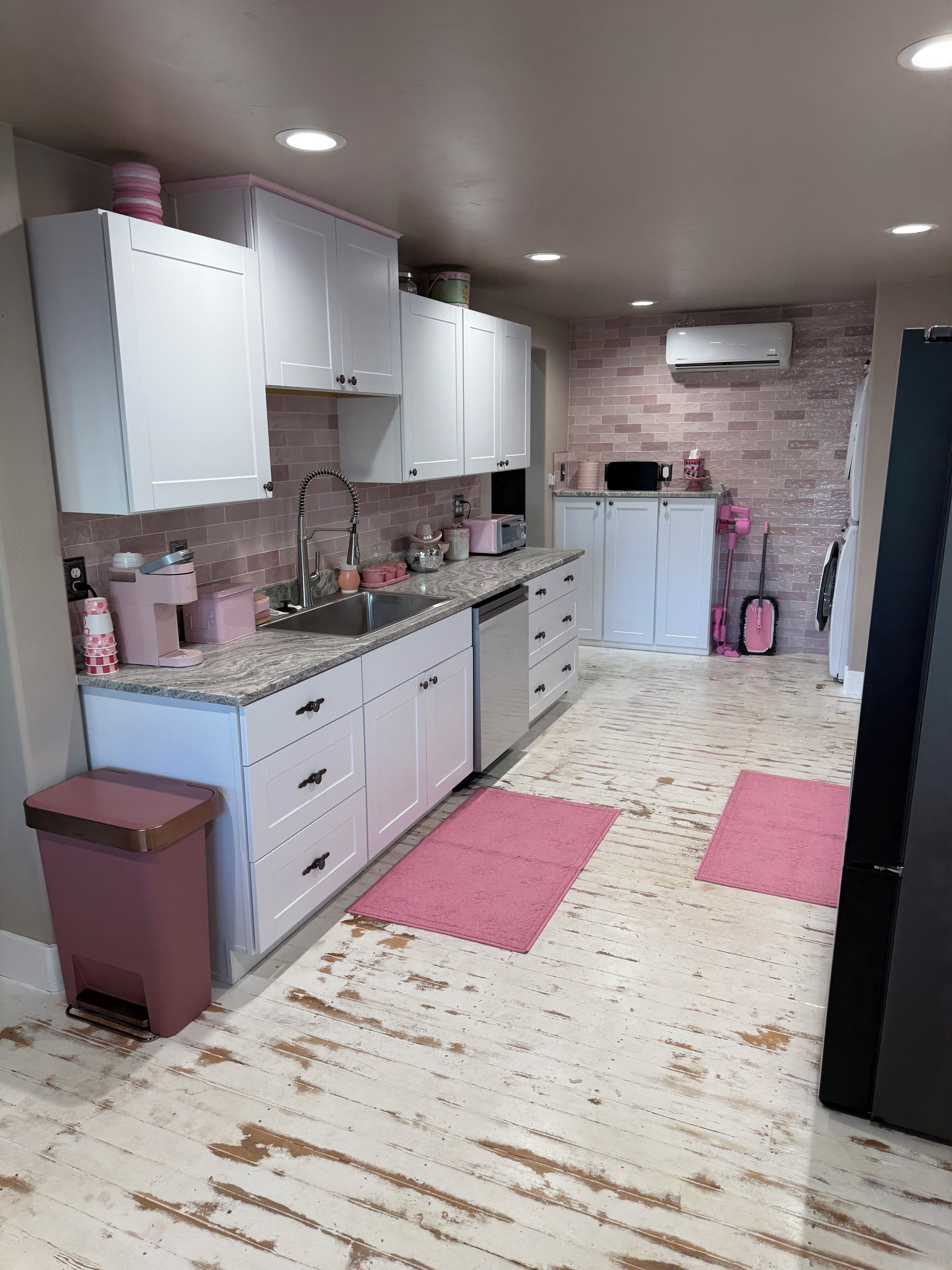 Et køkken med hvide skabe, en granitbordplade og pink detaljer.