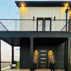 A modern two-story house with a balcony, a front door with a window, and a porch with a chair. - New Build! Modern Murfreesboro Townhome with Pool - 2BR/2.5BA - sleeps 6 (Murfreesboro)