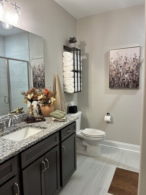 Un baño moderno con encimera de granito, muebles de color oscuro, inodoro y toallero de pared.