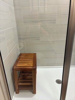 Ein Duschbereich mit einer hölzernen Sitzbank, gefliesten Wänden und einer Glastür.
