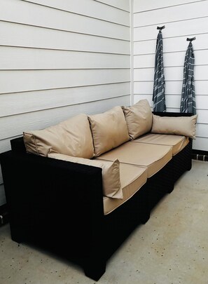 A black outdoor sofa with beige cushions against a white wooden wall, with two patterned cloths hanging on the wall. - New Build! Modern Murfreesboro Townhome with Pool - 2BR/2.5BA - sleeps 6 (Murfreesboro)
