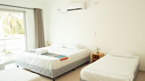 A hotel room with three beds, a small bedside table, a window with curtains, and an air conditioning unit on the wall. - Hotel Caribe Covenas (Tolú)