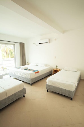A hotel room with three beds, a small bedside table, a window with curtains, and an air conditioning unit on the wall. - Hotel Caribe Covenas (Tolú)