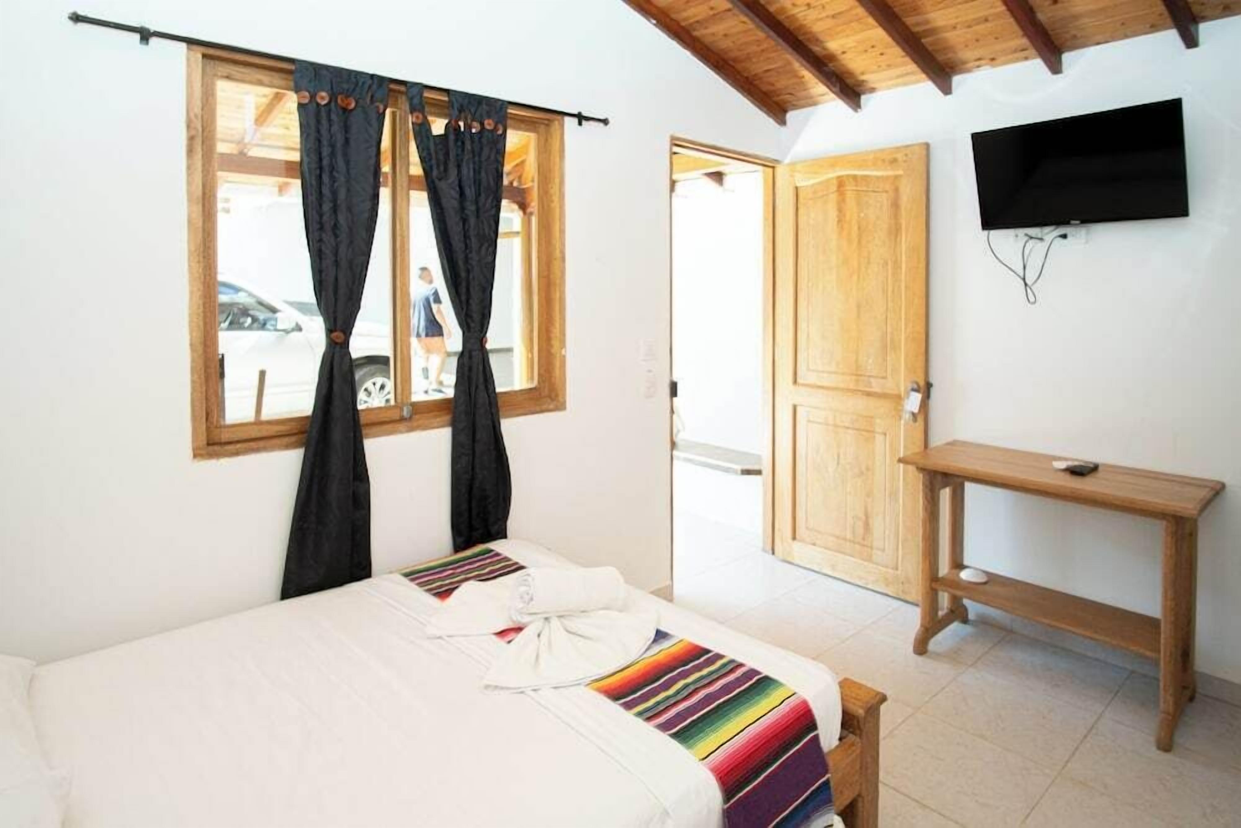 Une chambre à coucher avec un lit, un bureau en bois, une télévision et une fenêtre avec des rideaux.