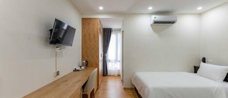 Habitación de hotel con escritorio de madera, televisor, dos camas y unidad de aire acondicionado.