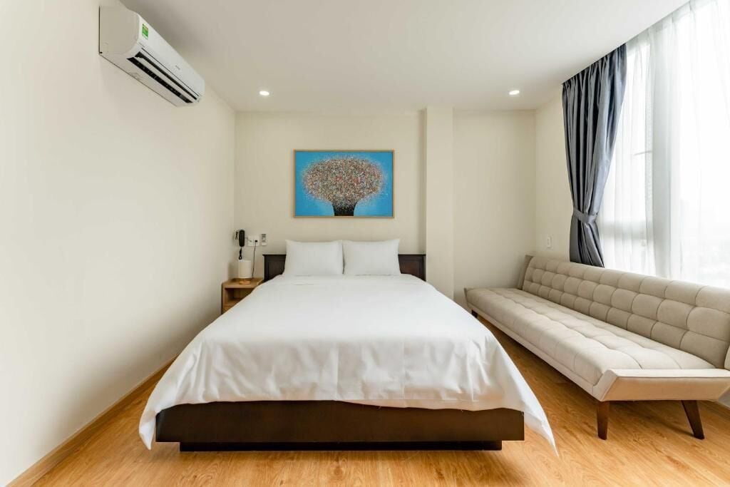 Een slaapkamer met een bed, nachtkastje, lamp, bank en een schilderij aan de muur.