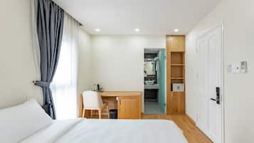 Habitación de hotel con cama, escritorio, silla, armario y baño visible a través de una puerta abierta.