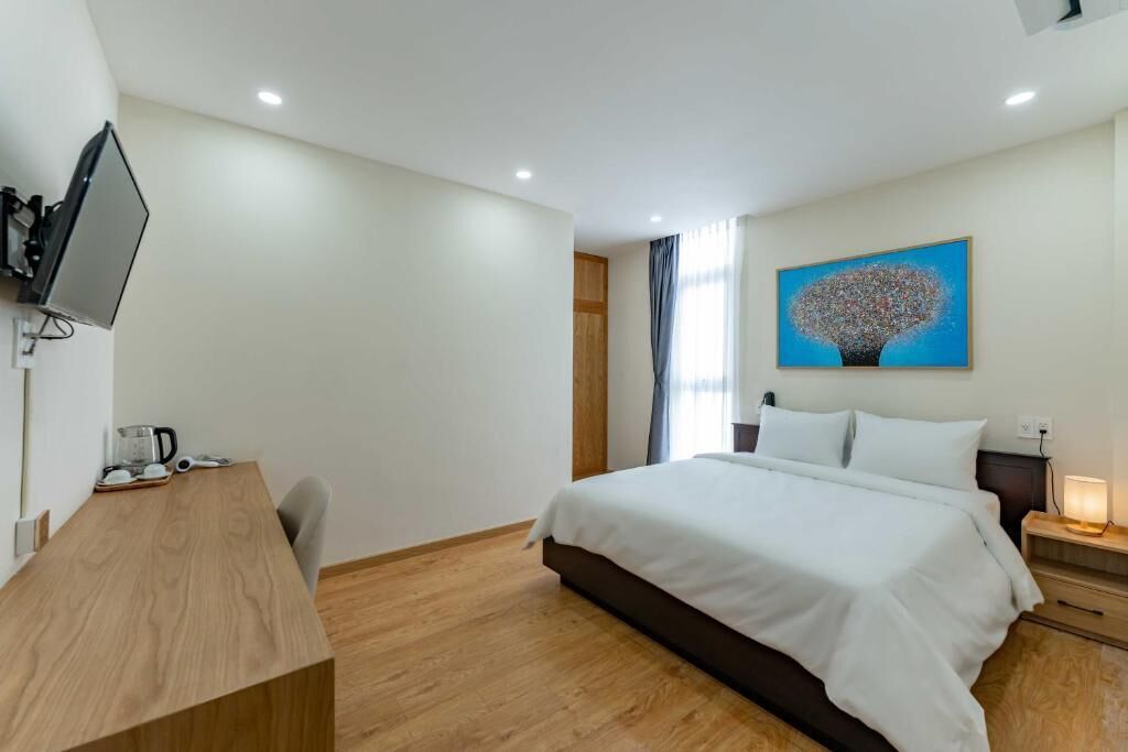 A hotel room with a bed, a desk, a television, and a painting on the wall.