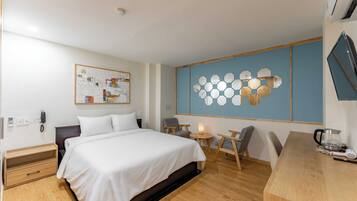 Ein Hotelzimmer mit Bett, Nachttisch, Stuhl, Schreibtisch und einem an der Wand montierten Fernseher.