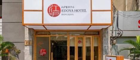La entrada del HOTEL EDOYA, con fachada moderna, un mostrador de recepción a la vista y una puerta de vidrio transparente.