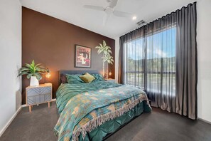 A bedroom with a bed, a nightstand, a potted plant, a wall art piece, and a window with curtains. - Coronation Station (Alpine)