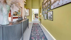 A hallway with a patterned carpet, a decorative vase, and a wall adorned with framed photographs. - Coronation Station (Alpine)
