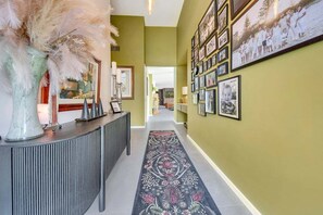 A hallway with a patterned carpet, a decorative vase, and a wall adorned with framed photographs. - Coronation Station (Alpine)