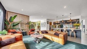 A modern living room with a sofa, coffee table, and a kitchen area in the background. - Coronation Station (Alpine)