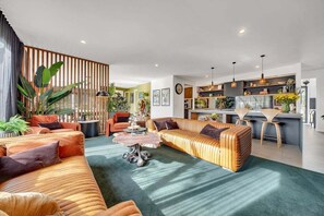 A modern living room with a sofa, coffee table, and a kitchen area in the background. - Coronation Station (Alpine)
