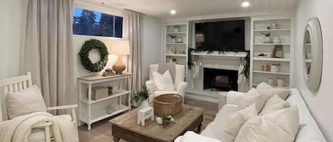Un salon avec une cheminée, des meubles blancs et un téléviseur.