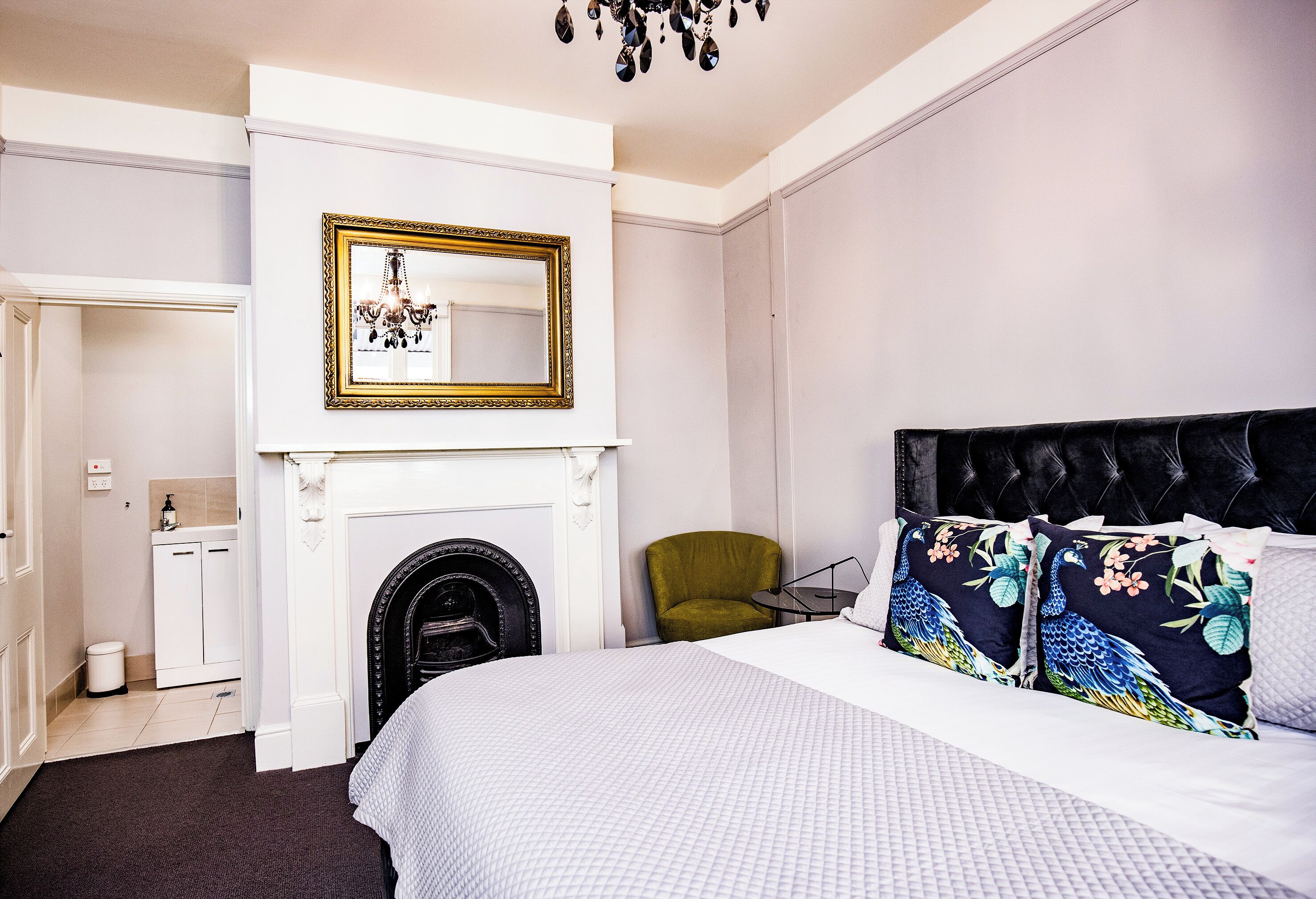 Una habitación de hotel con cama, un sillón verde, una chimenea y un espejo con marco decorativo.