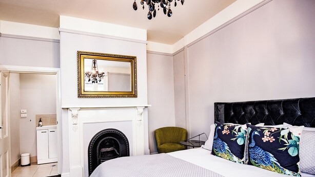 A hotel room with a bed, a green armchair, a fireplace, and a mirror with a decorative frame. - Welcome to the House of Ferment. Walk to everything in Orange (Orange)