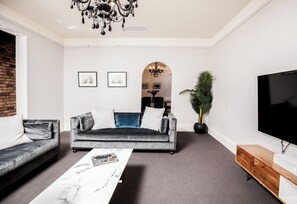 Ein Wohnzimmer mit grauem Sofa, einem weißen Couchtisch, einem Fernseher und einer Deckenleuchte.
