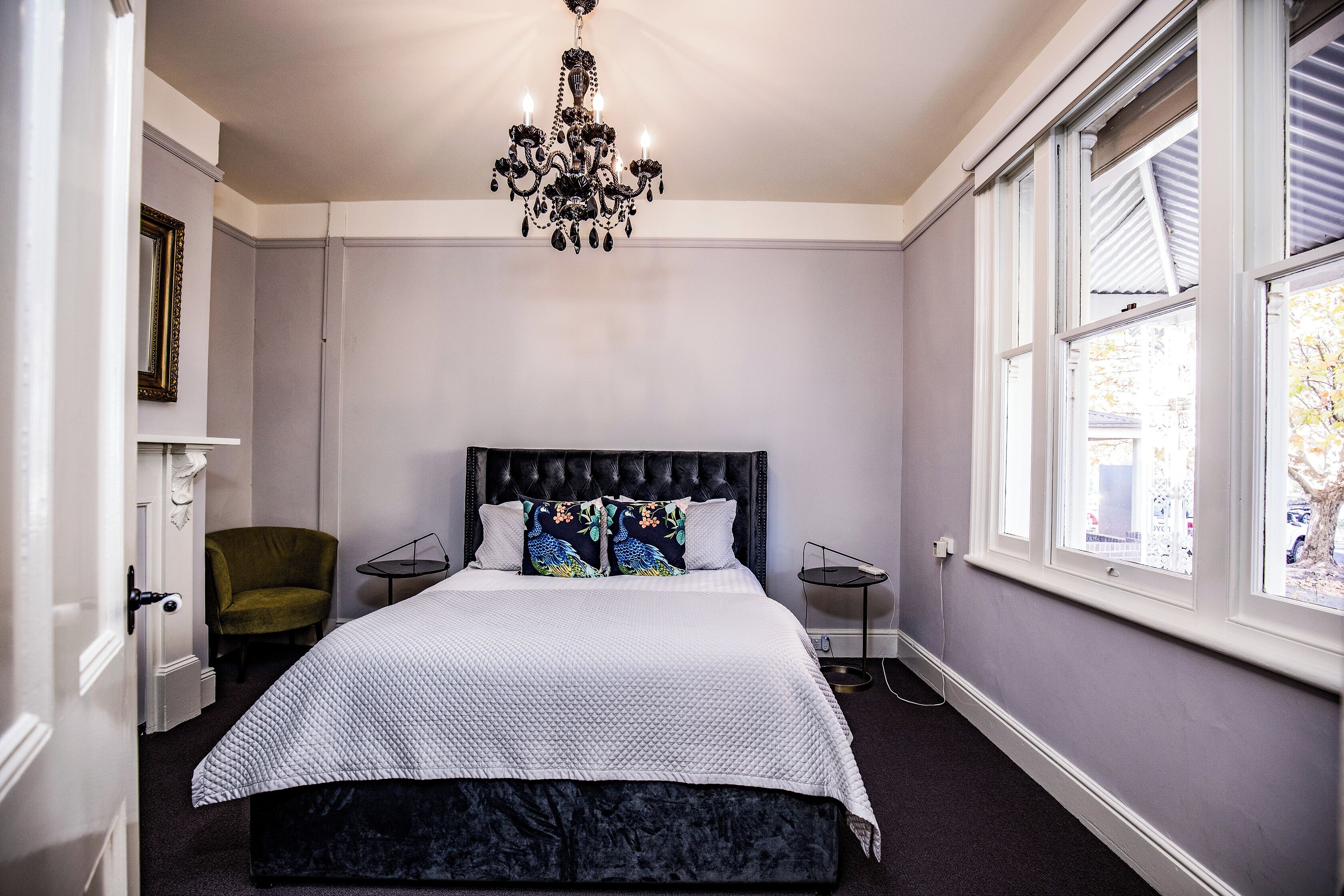 A bedroom with a bed, a chair, a table, a chandelier, and a window.