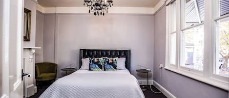 Un dormitorio con cama, una silla, una mesa, una araña y una ventana.